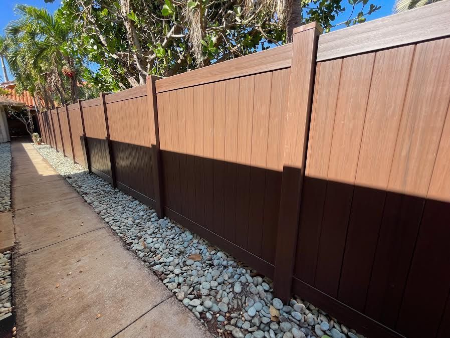 A wooden fence is sitting next to a sidewalk with rocks.