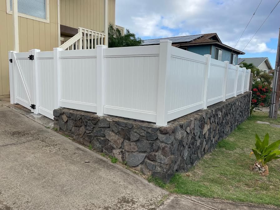 A white fence is sitting on top of a stone wall next to a house.