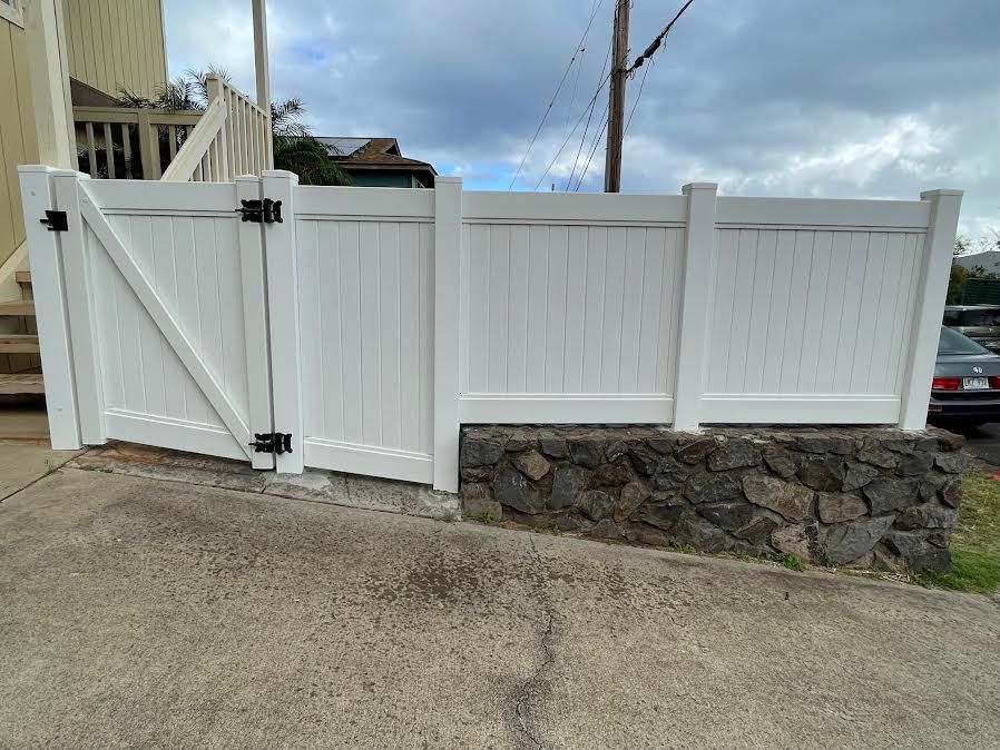 A white fence with a gate is sitting next to a stone wall.
