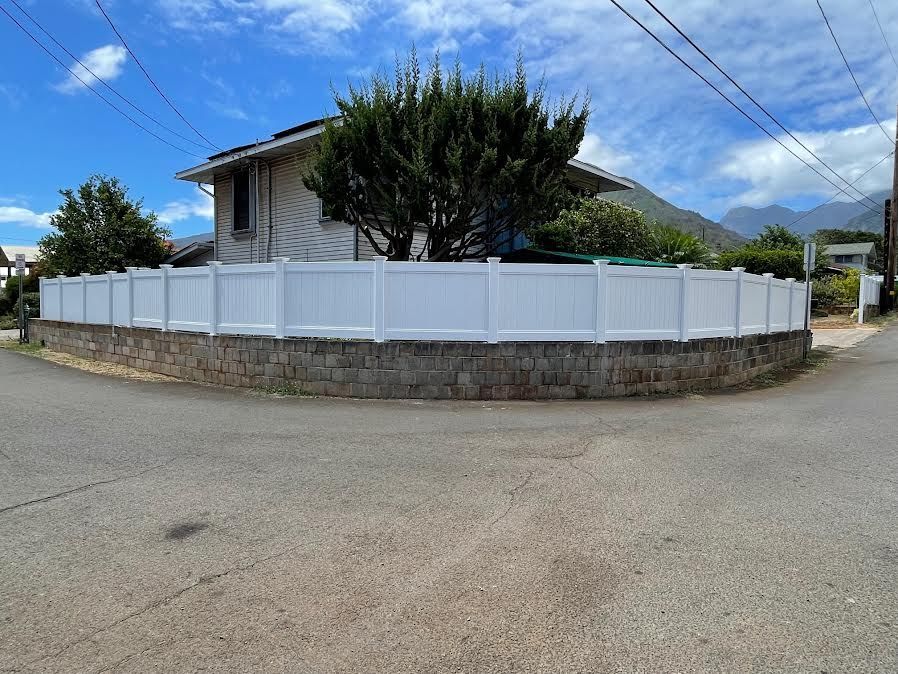A white fence surrounds a stone wall in front of a house.
