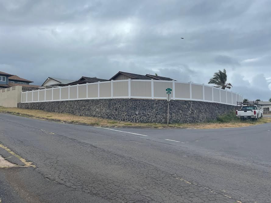A white fence is surrounding a stone wall on the side of a road.