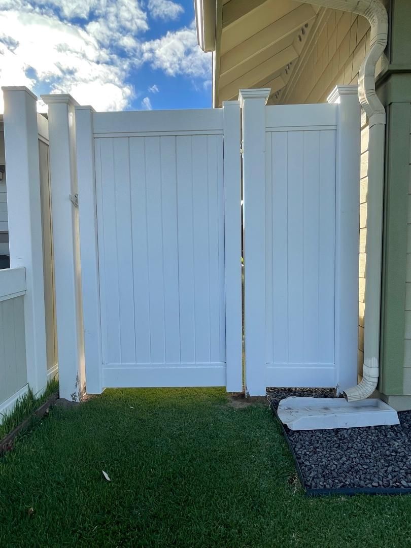 A white fence with a gate in the backyard of a house.