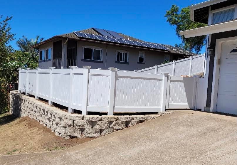 A white fence surrounds a house with solar panels on the roof.