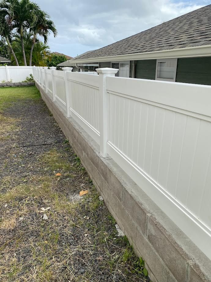 A white fence is surrounding a brick wall in front of a house.