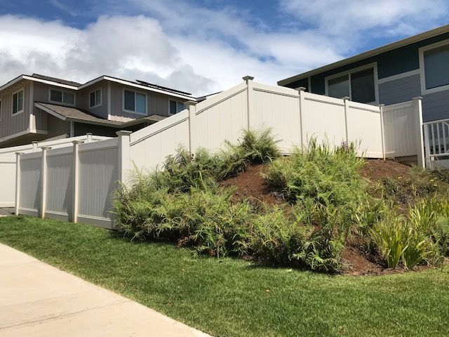 A white fence surrounds a grassy hill in front of a house.
