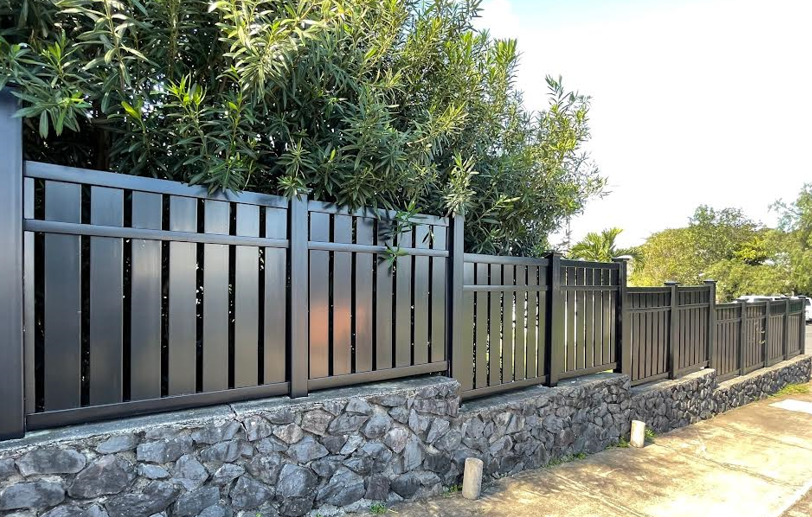 A black vinyl fence is surrounded by trees and a stone wall.