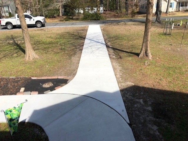 A white truck is parked on the side of the road next to a concrete walkway.
