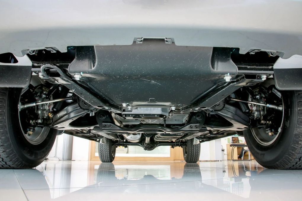 Underside of a red car, showing black chassis components on a metal ramp.