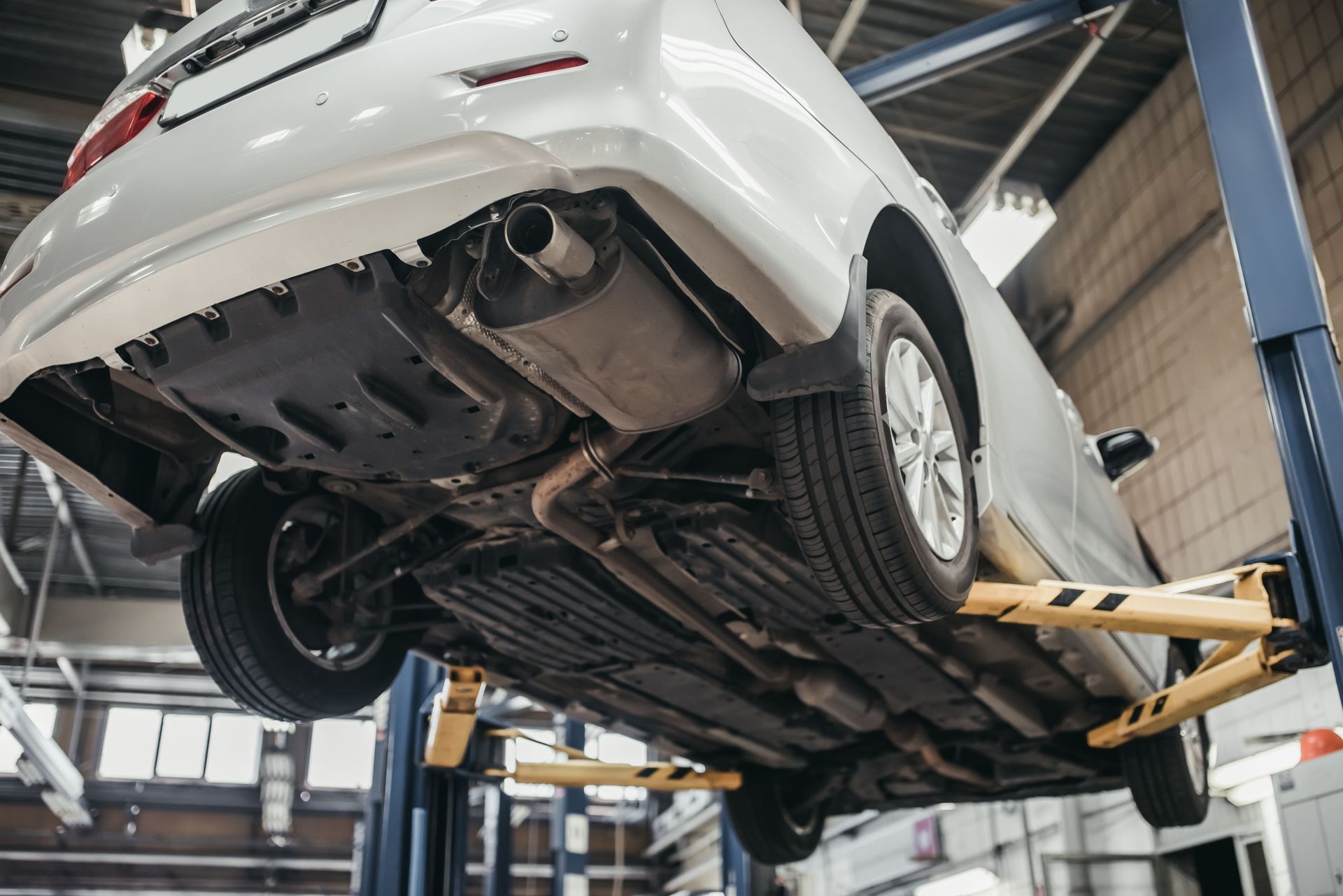 A car on a lift in a repair shop, seen from below.