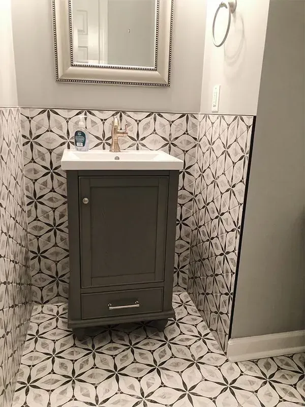 Bathroom with gray vanity, white sink, patterned tile, and gold faucet.