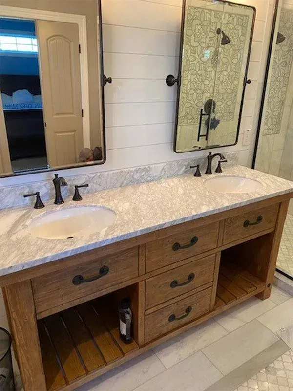 Bathroom vanity with two sinks, a wooden cabinet, two mirrors, and a light-colored countertop.