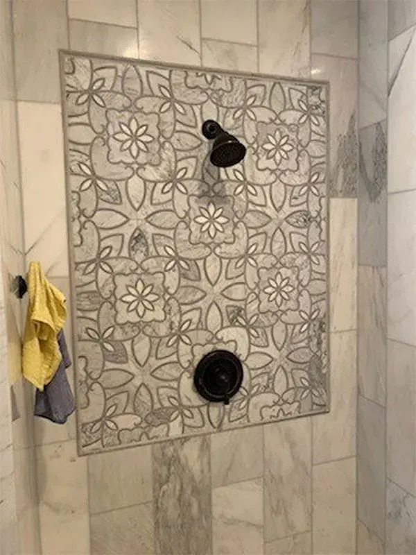 Shower with patterned gray and white tile focal wall, black showerhead and controls.
