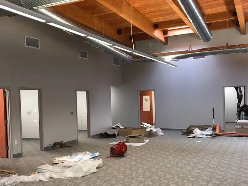 Empty room with gray walls, wood ceiling, and multiple doorways. Construction debris on the floor.