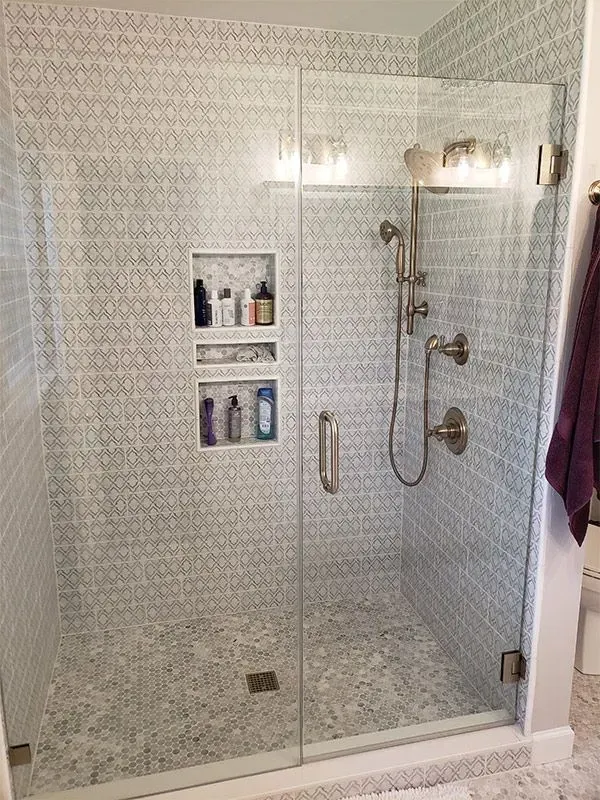 Modern shower with glass door, mosaic tile walls, and recessed shelves holding toiletries.