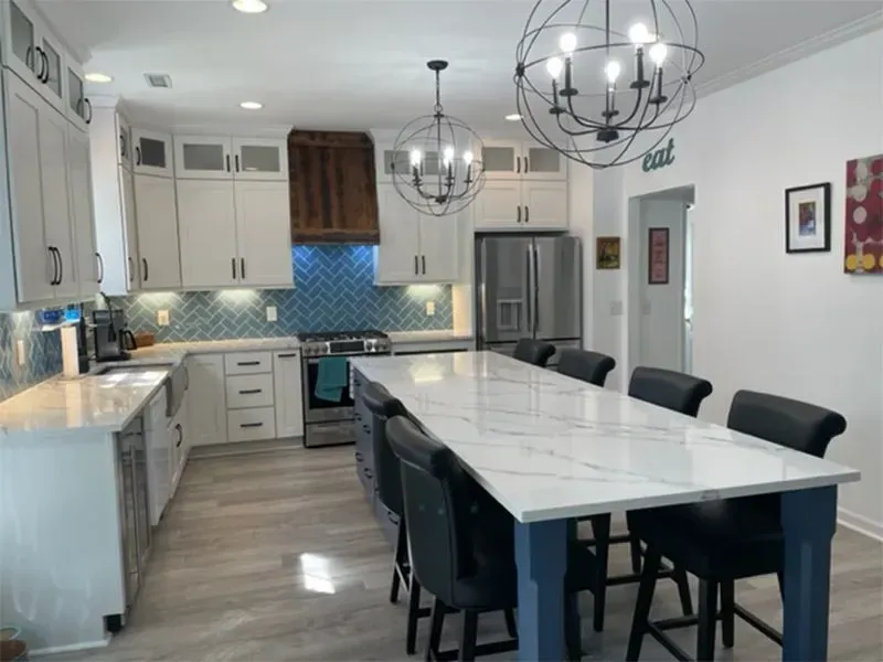 Spacious kitchen with a long white countertop island and blue cabinets.  Modern design, and lots of seating.