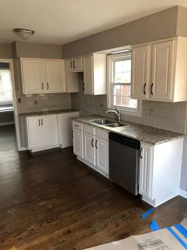Newly renovated kitchen with white cabinets, gray countertops, and stainless steel dishwasher on dark wood floors.