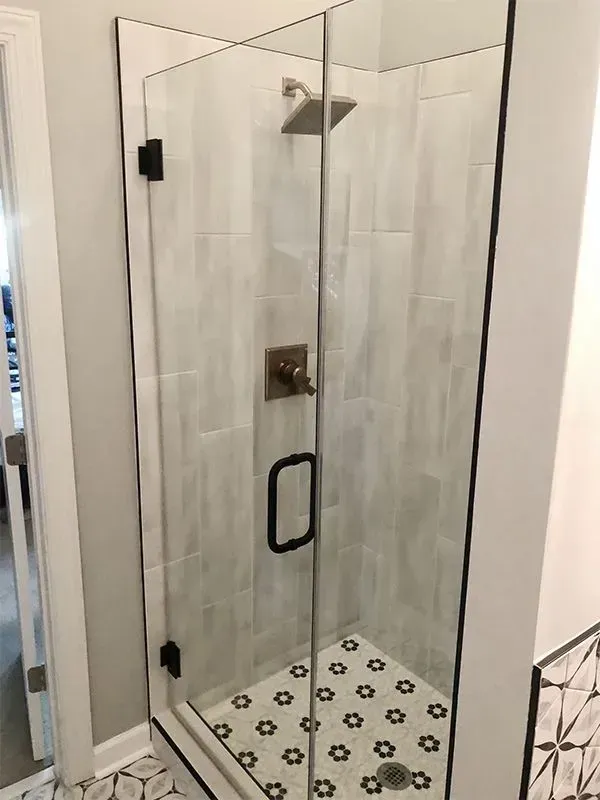 Glass shower enclosure with black hardware, white and gray tile walls and floor.