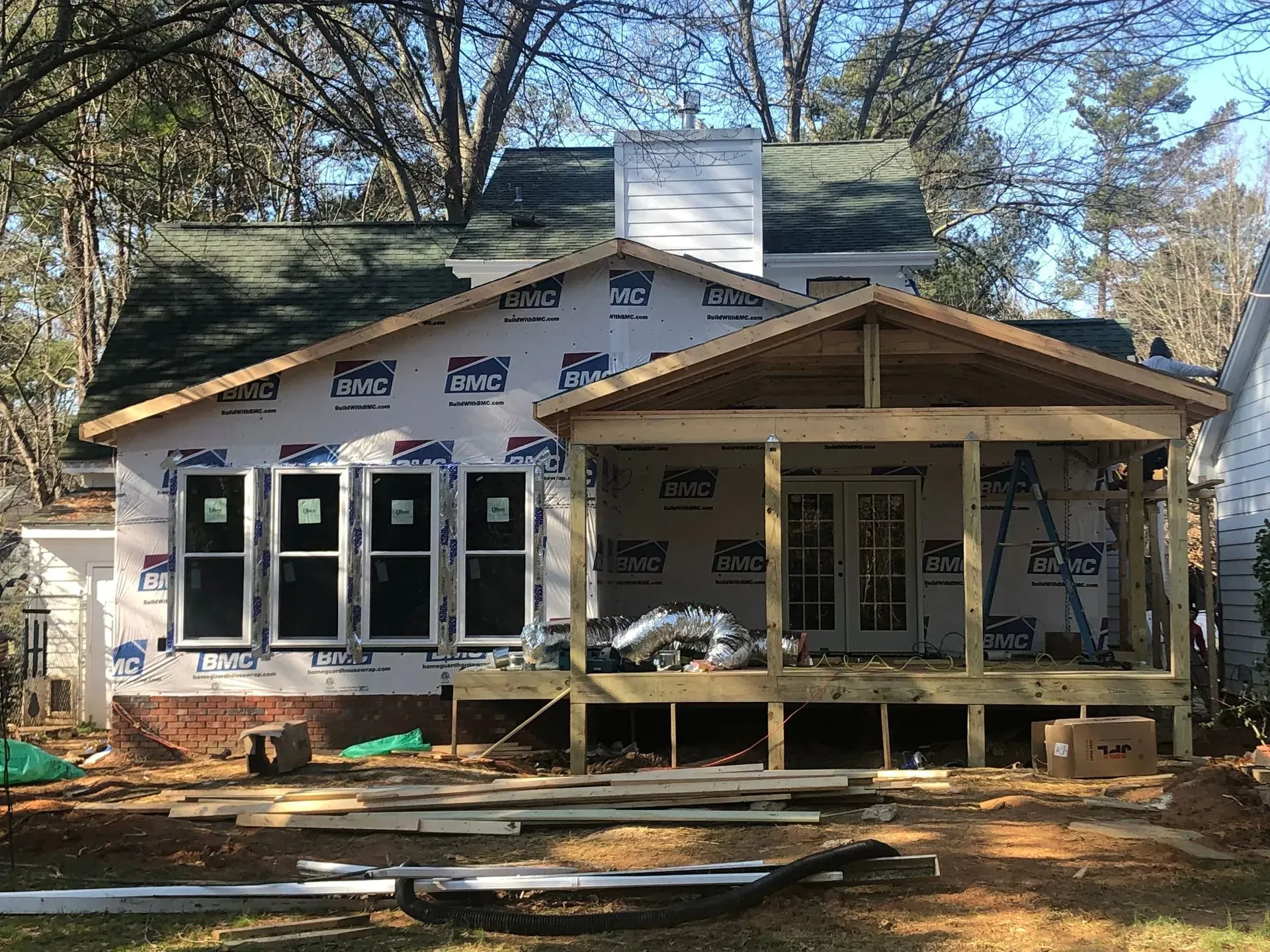 Construction of a house addition with new windows and a screened porch on a sunny day.