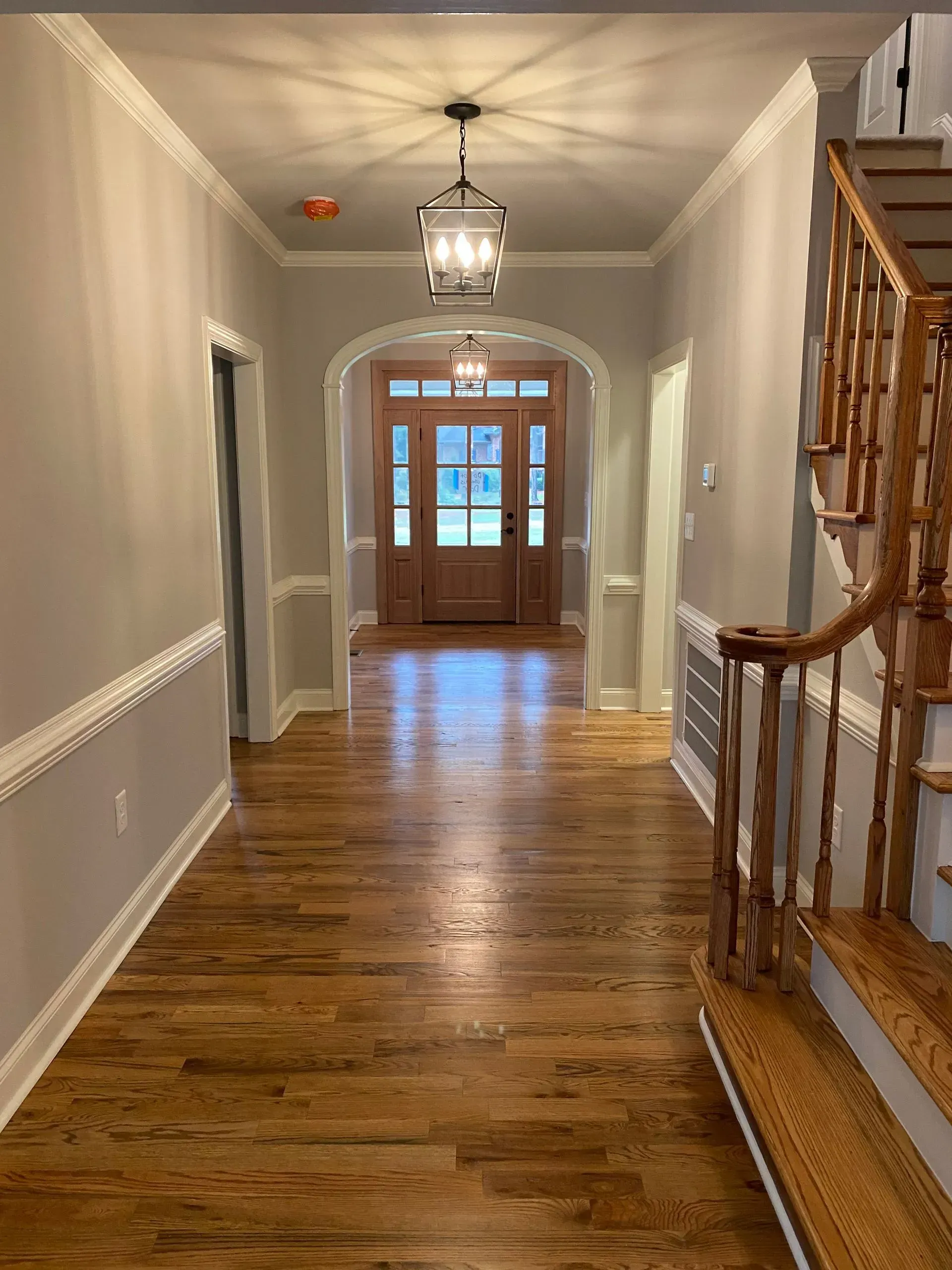 Hallway with wood floors, neutral walls, trim, and light fixtures leading to a front door.