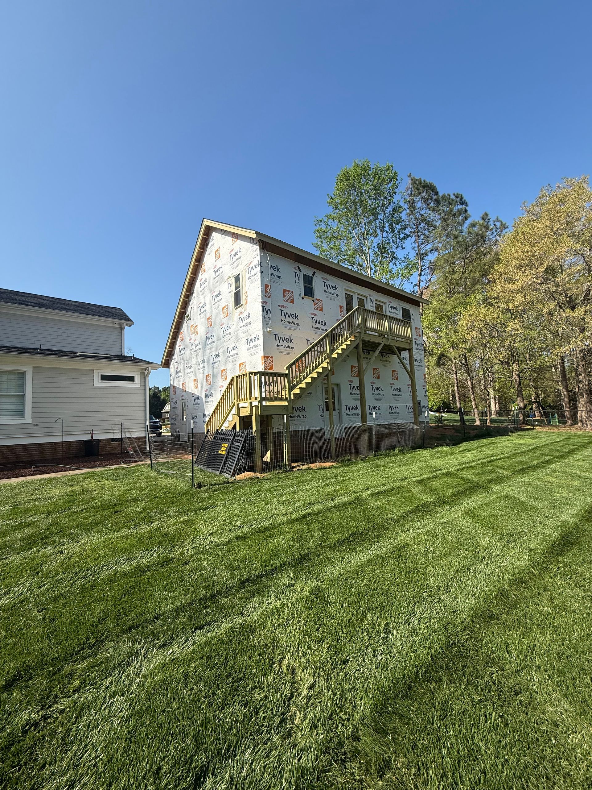 A white two-story house with a climbing wall on its exterior side and a wooden staircase in a grassy yard under a blue sky.