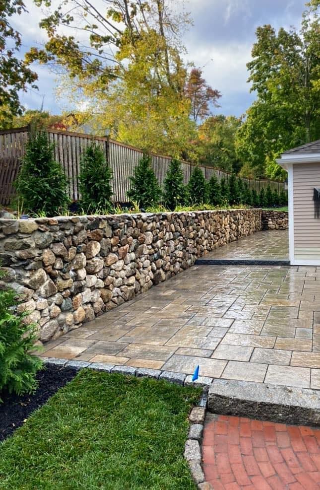 a stone wall surrounds a brick walkway leading to a house