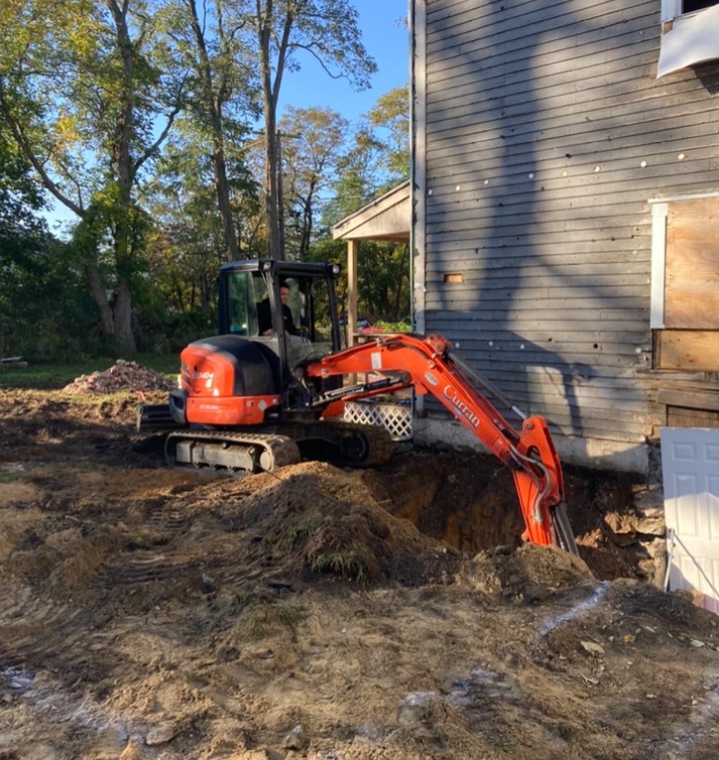 a small orange excavator is digging a hole in front of a house