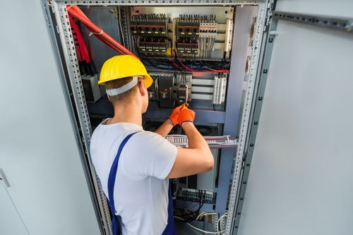 Technician in hard hat working inside an electrical control panel cabinet