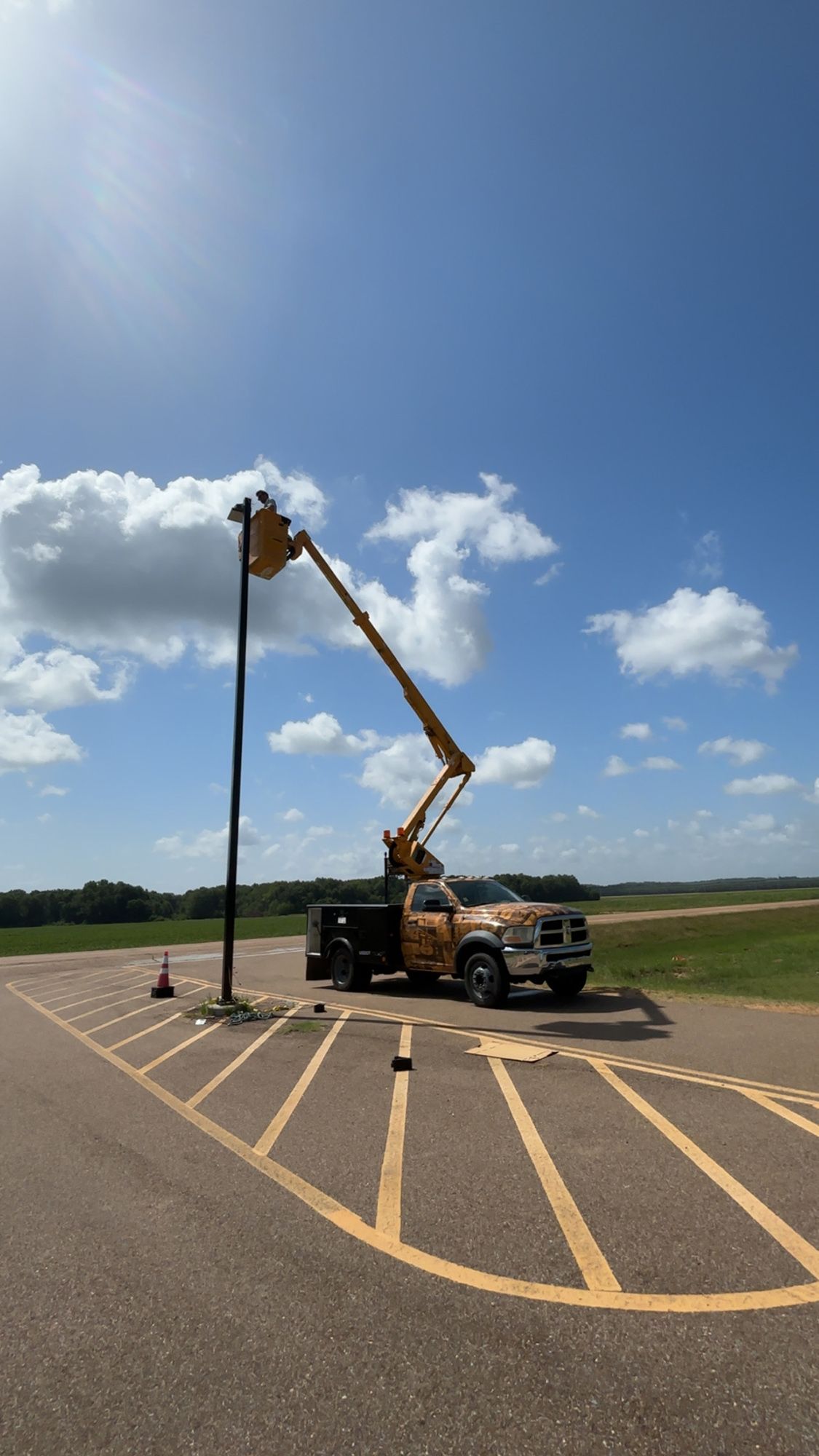 Utility truck with extended boom lifting a pole in a sunny parking lot under a blue sky