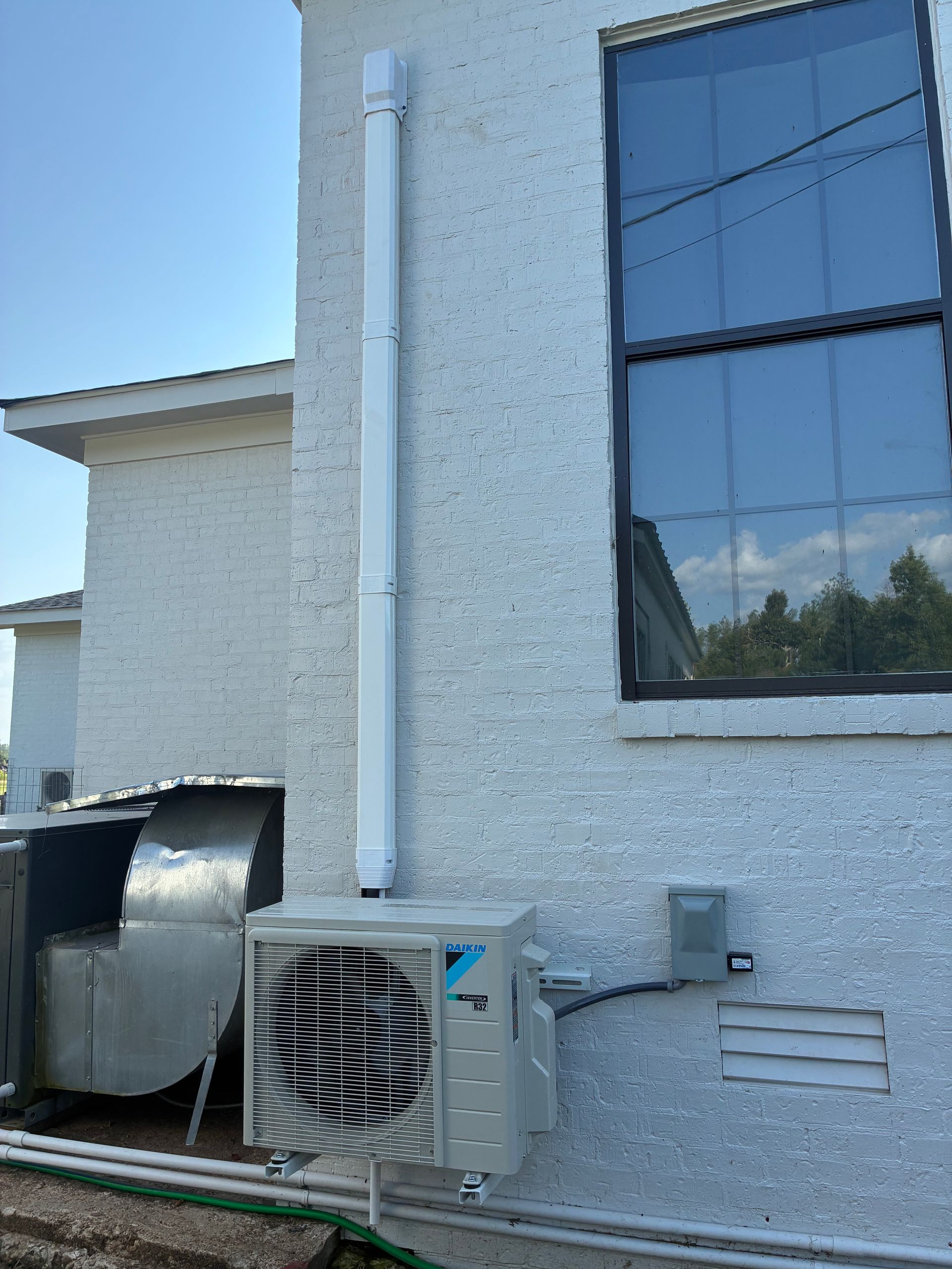 White stucco building exterior with a large window, wall-mounted HVAC unit, and vented equipment beside it.