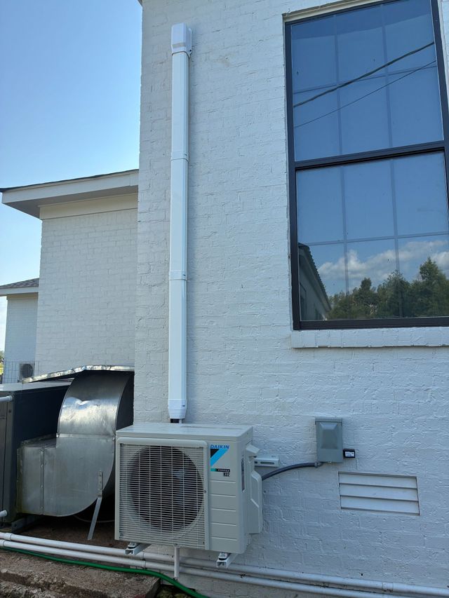 White building wall with windows, HVAC unit, and ductwork outside under a blue sky