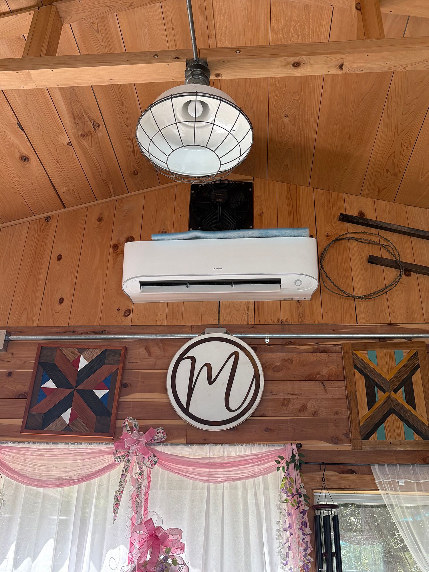 Wooden interior wall with a hanging round clock, white air conditioner, and decorative signs above a curtained window.