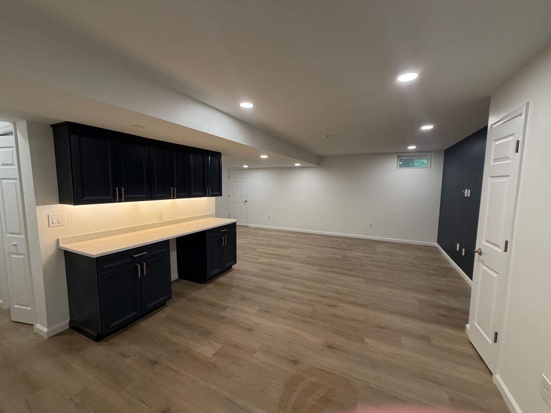 Empty room with wood floors, recessed lights, and black cabinets along the left wall.