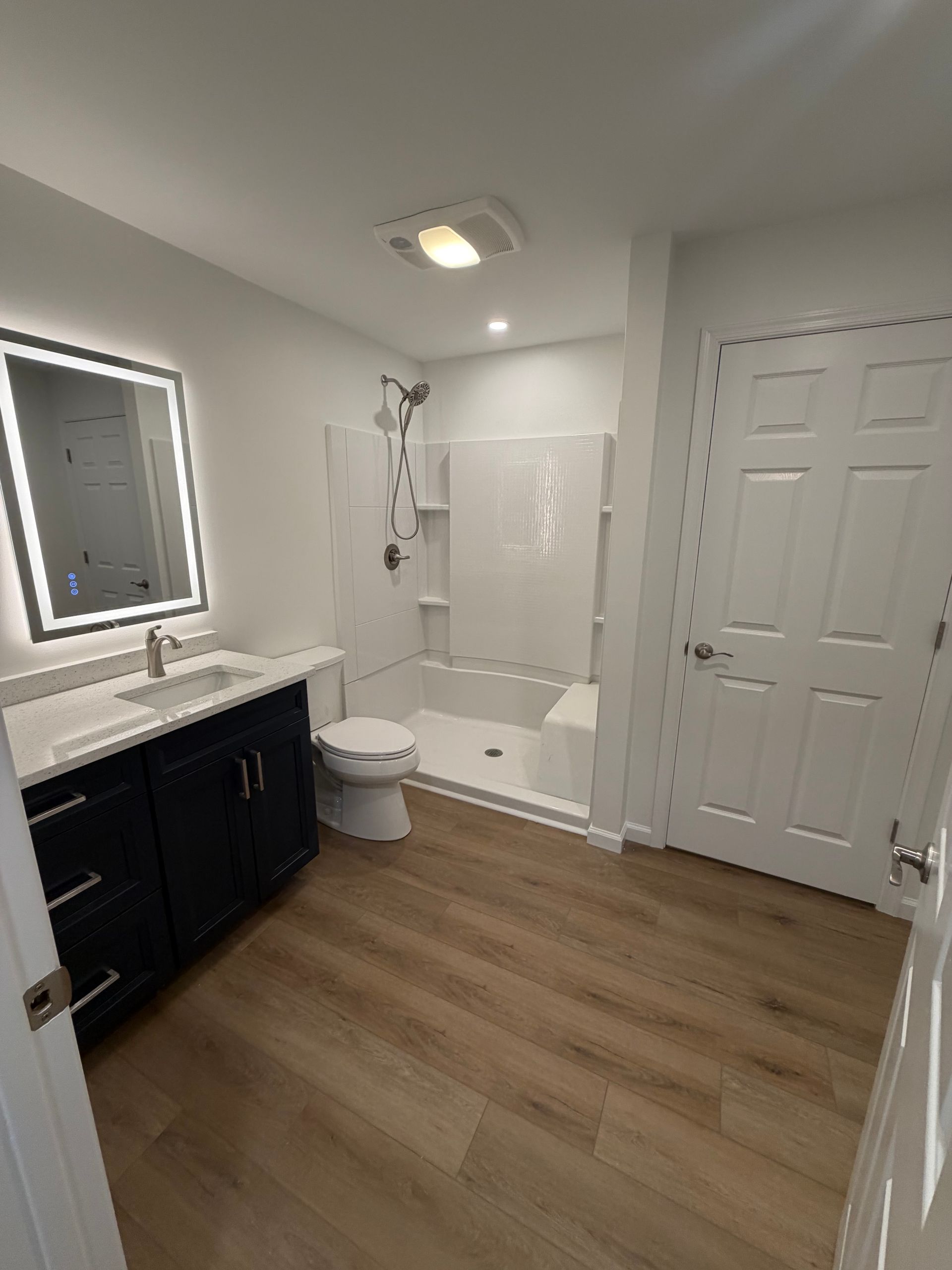 Bright bathroom with vanity, lit mirror, toilet, tub-shower, and white closet doors.