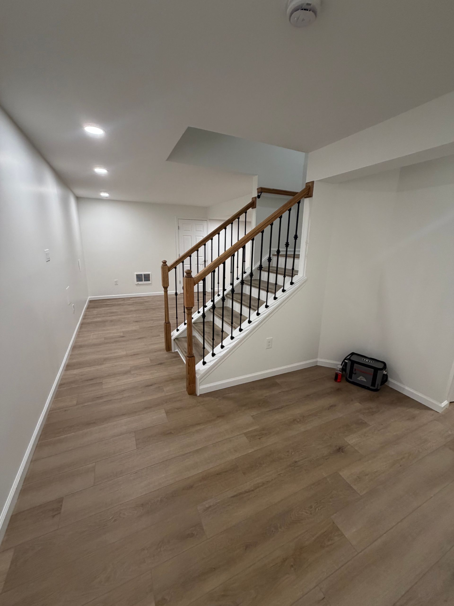 Empty room with wood floors, white walls, and a staircase with wooden railing.