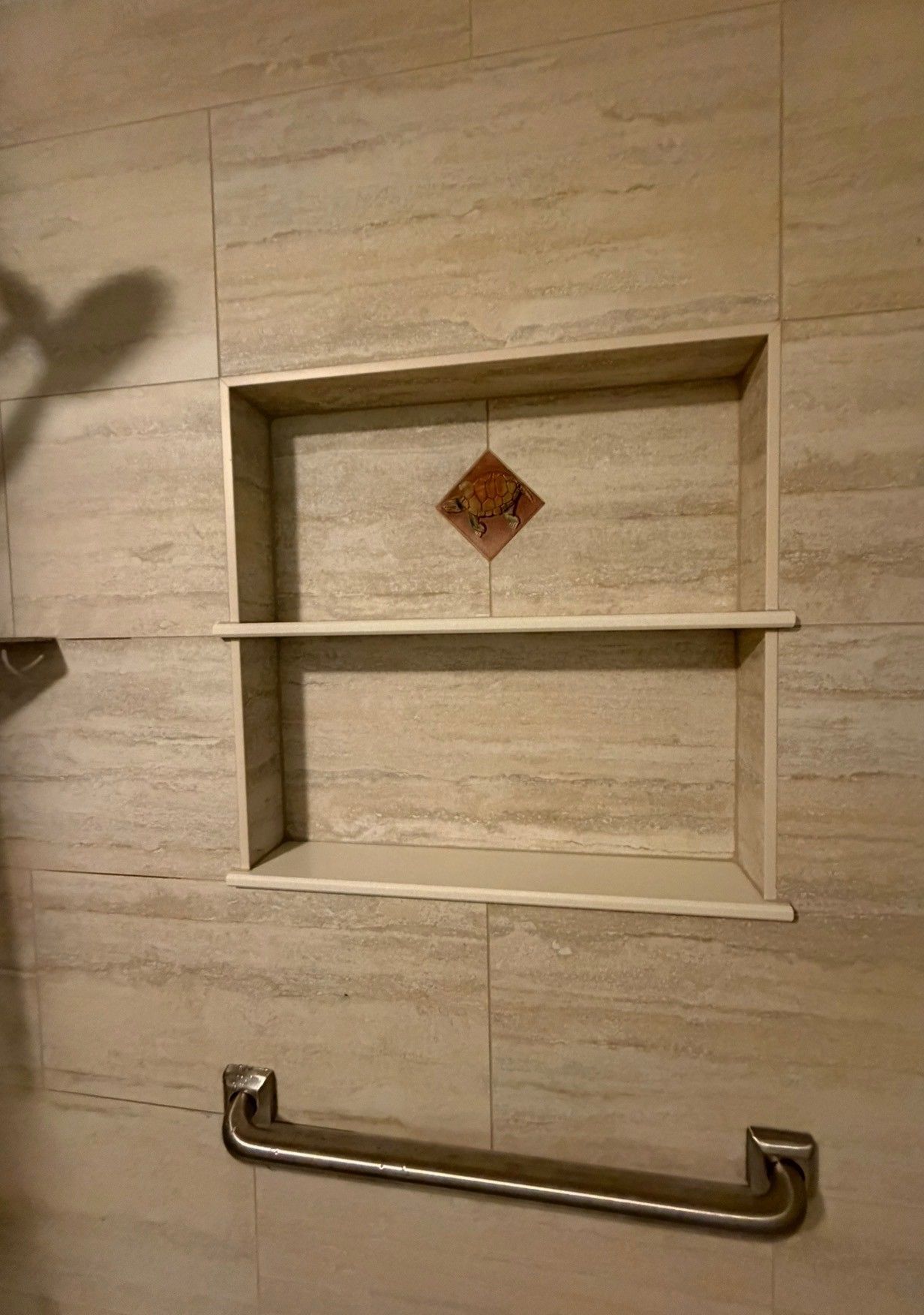 Bathroom wall niche with shelves and a metal grab bar on a beige tiled wall.