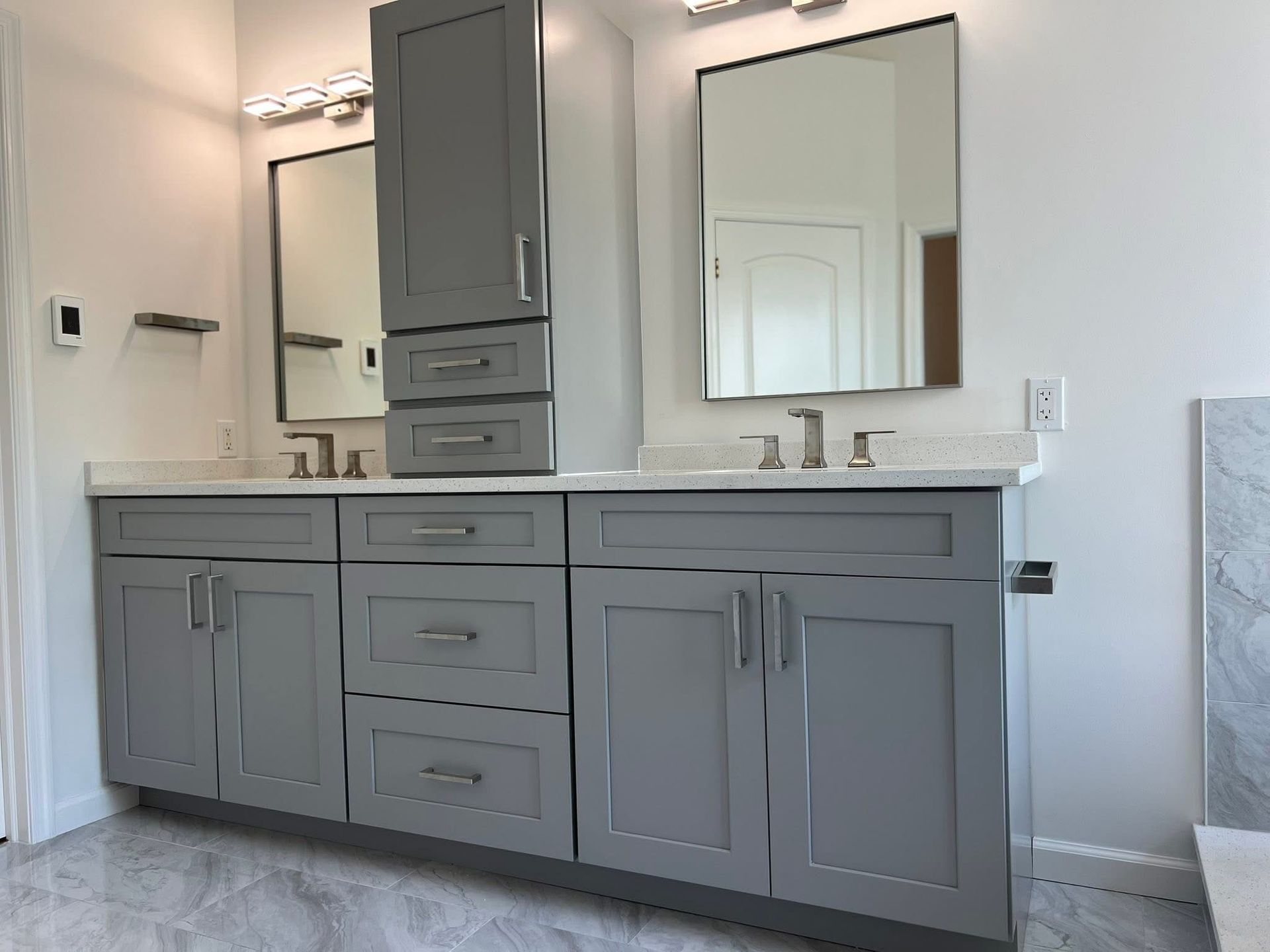 A bathroom with two sinks , two mirrors , and gray cabinets.