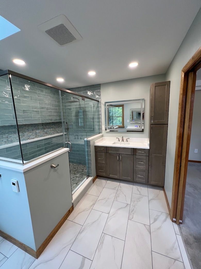 A bathroom with a sink , mirror and walk in shower.