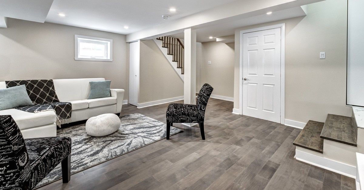 Finished basement living area with a white sofa, patterned armchairs, and gray flooring.