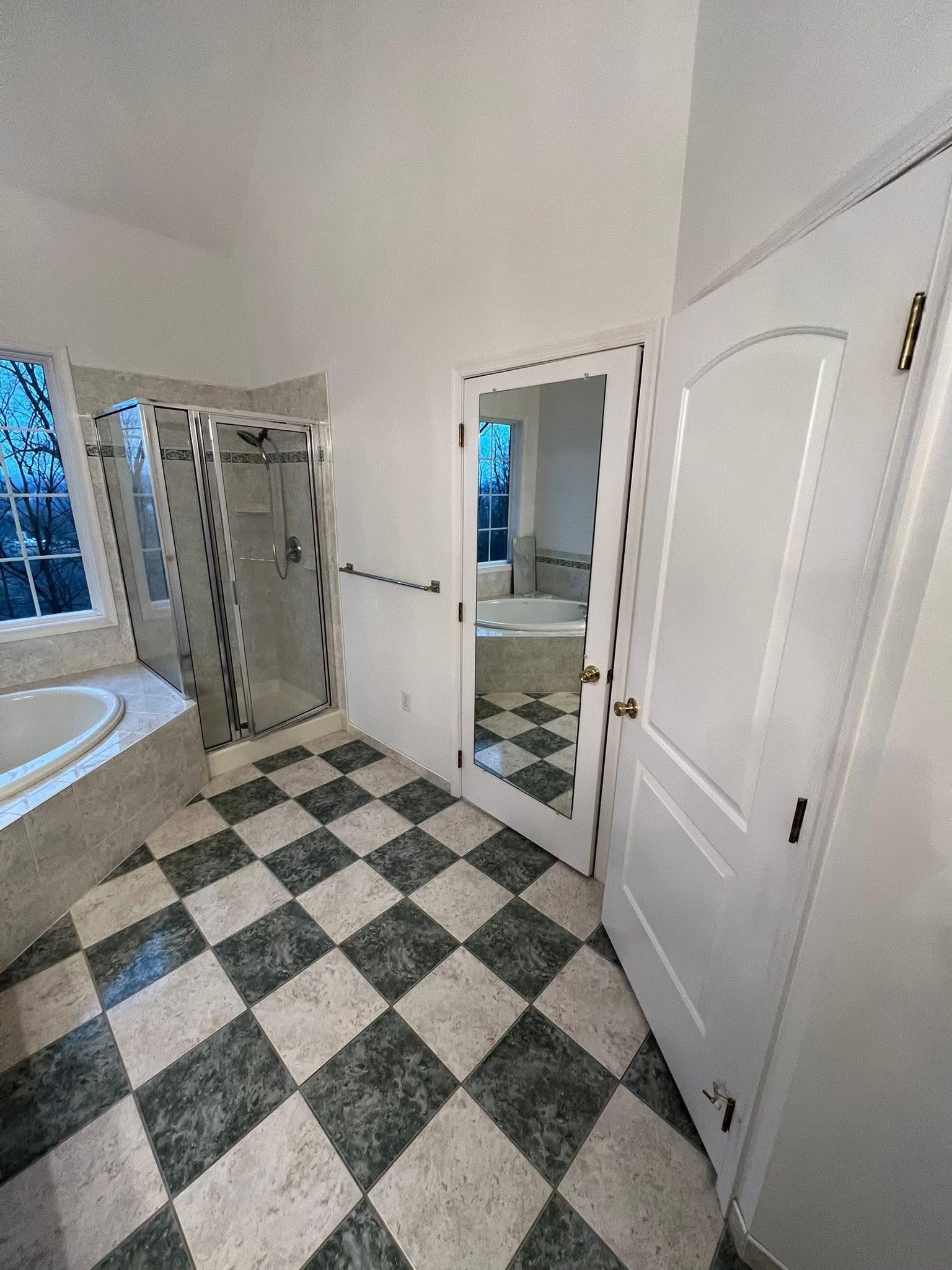 A bathroom with a black and white checkered floor, a shower, a bathtub, and a door leading to another room.