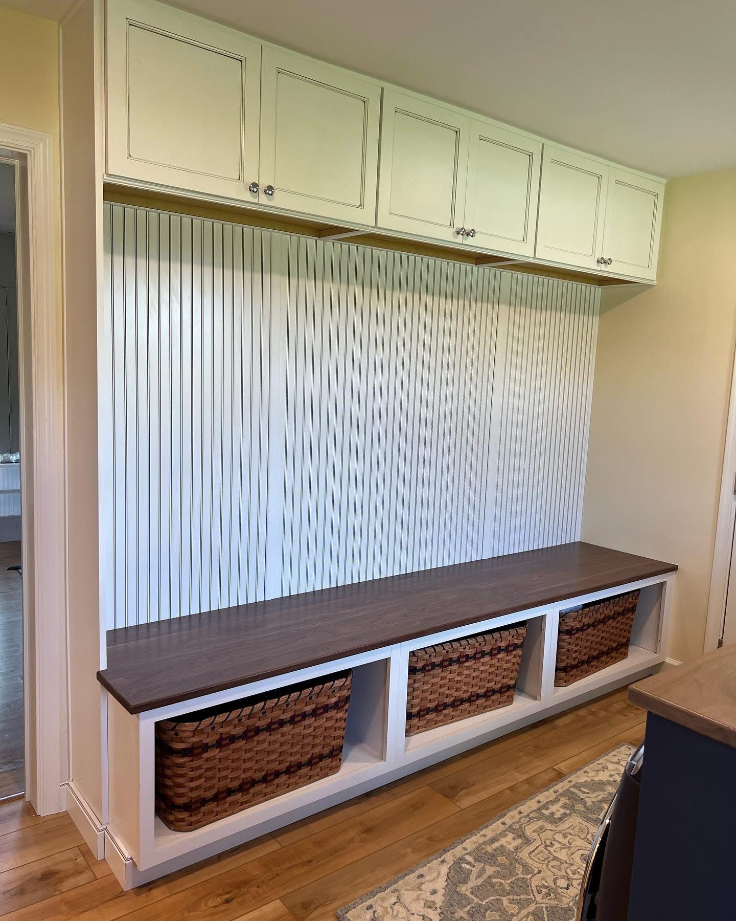 Built-in mudroom storage: white cabinets, bench with baskets, and abstract wall design.