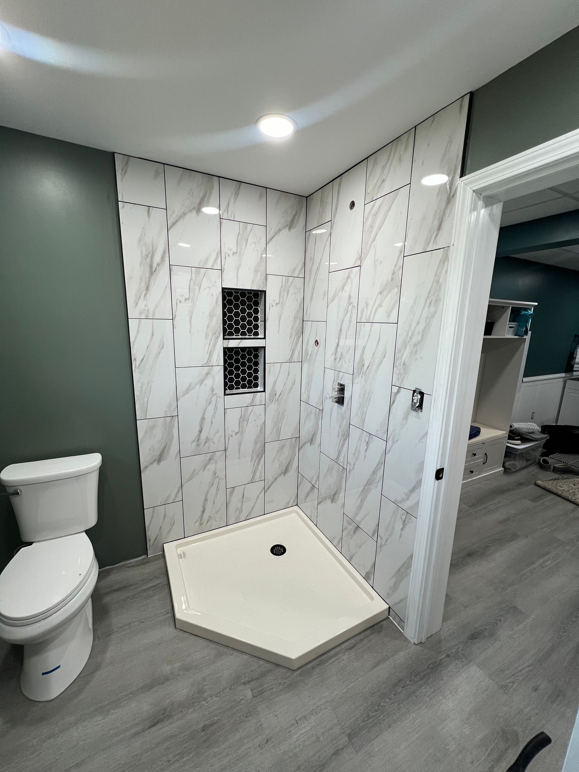 Bathroom with marble-look tiled shower, a white toilet, and green walls. Gray flooring and a pentagonal shower base.
