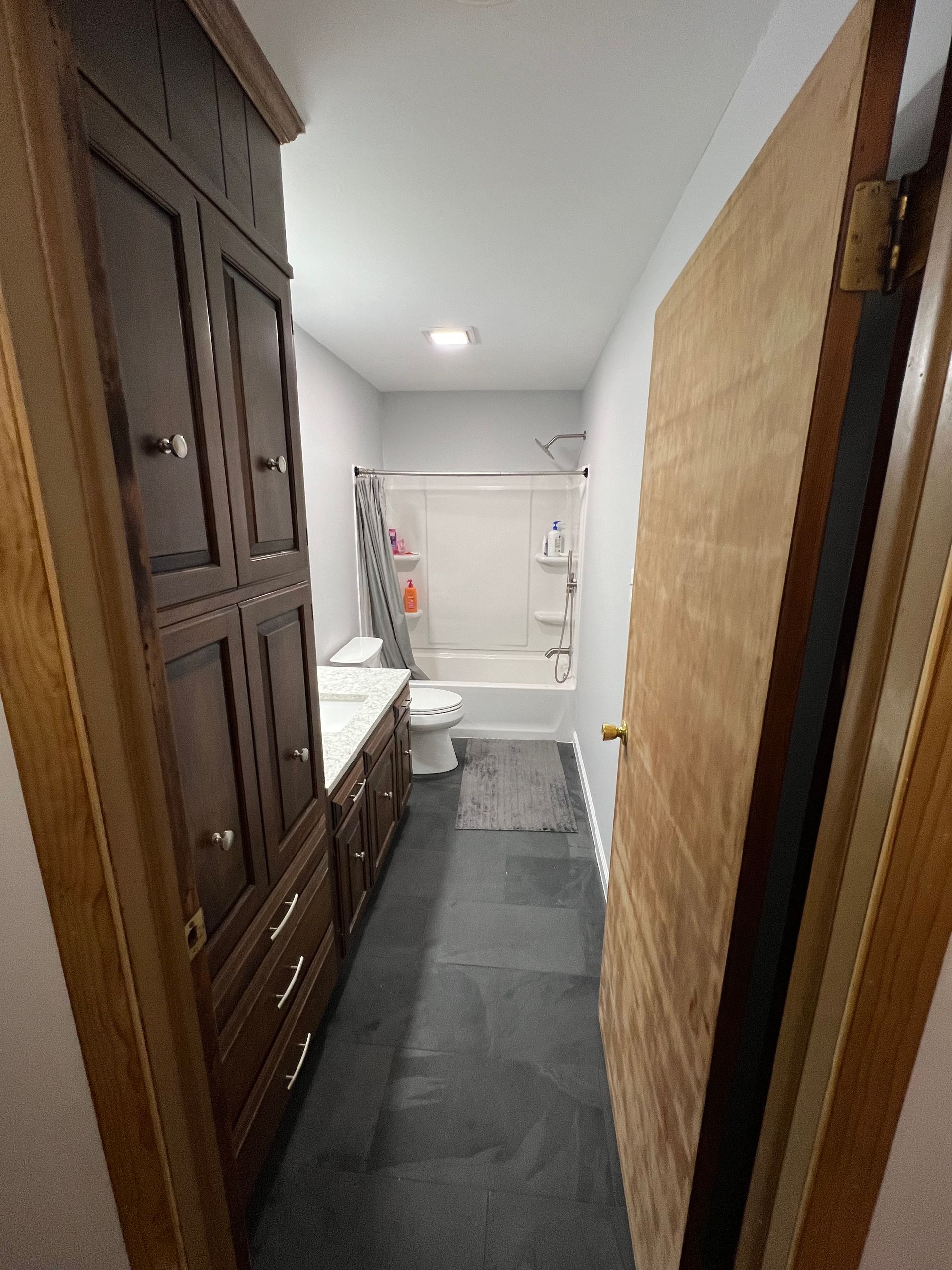 Narrow bathroom with dark cabinets, gray walls, and a closed wooden door on the right.