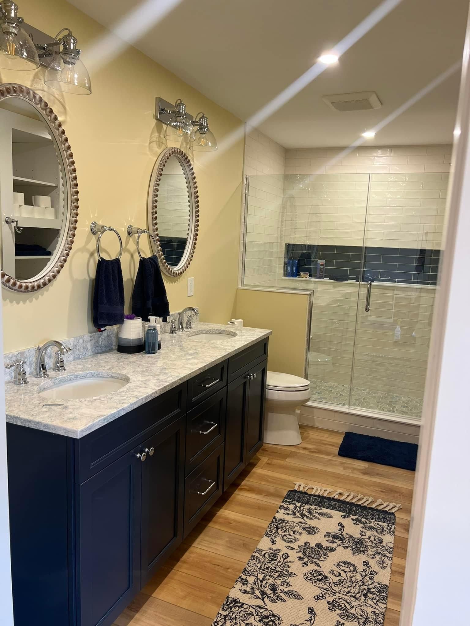Bathroom with dark blue vanity, two mirrors, and a glass shower.