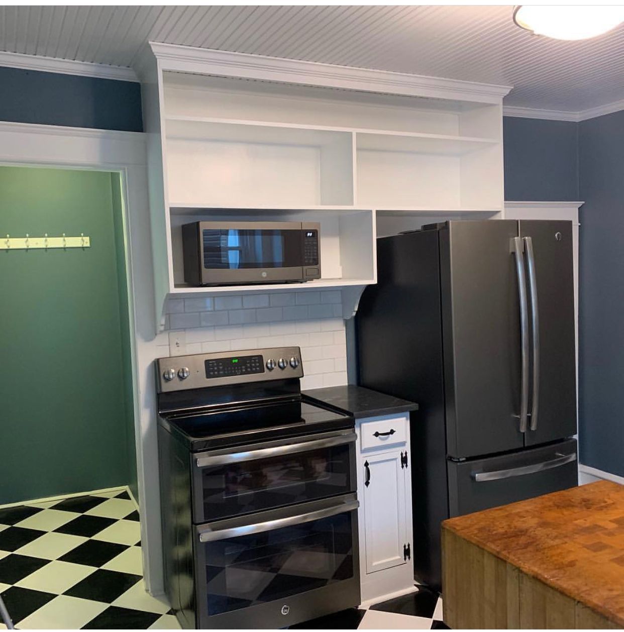 Kitchen with stainless steel appliances, white shelves, and checkerboard floor.