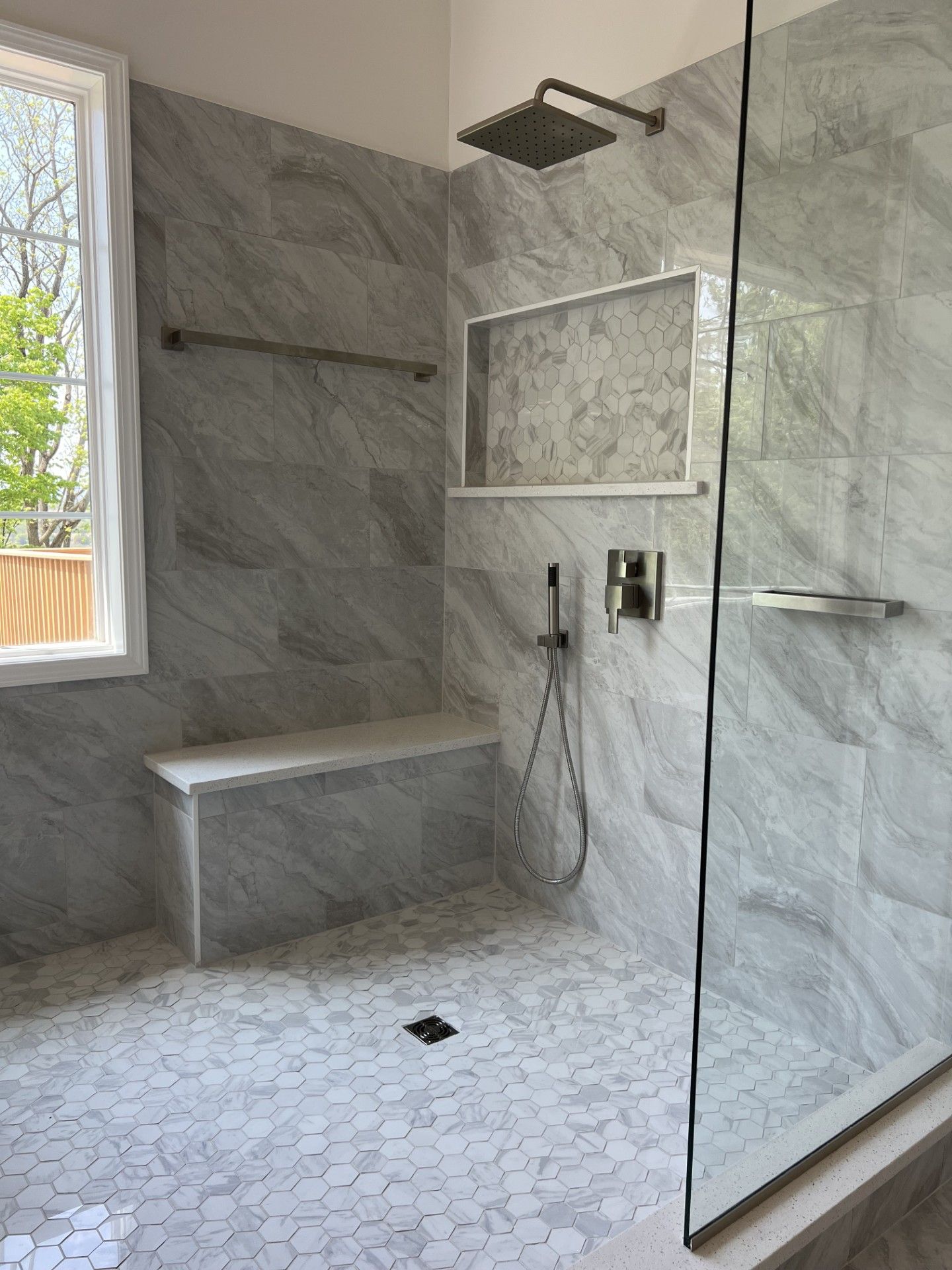 Modern bathroom with white and gray marble tile shower, built-in bench, and glass enclosure.