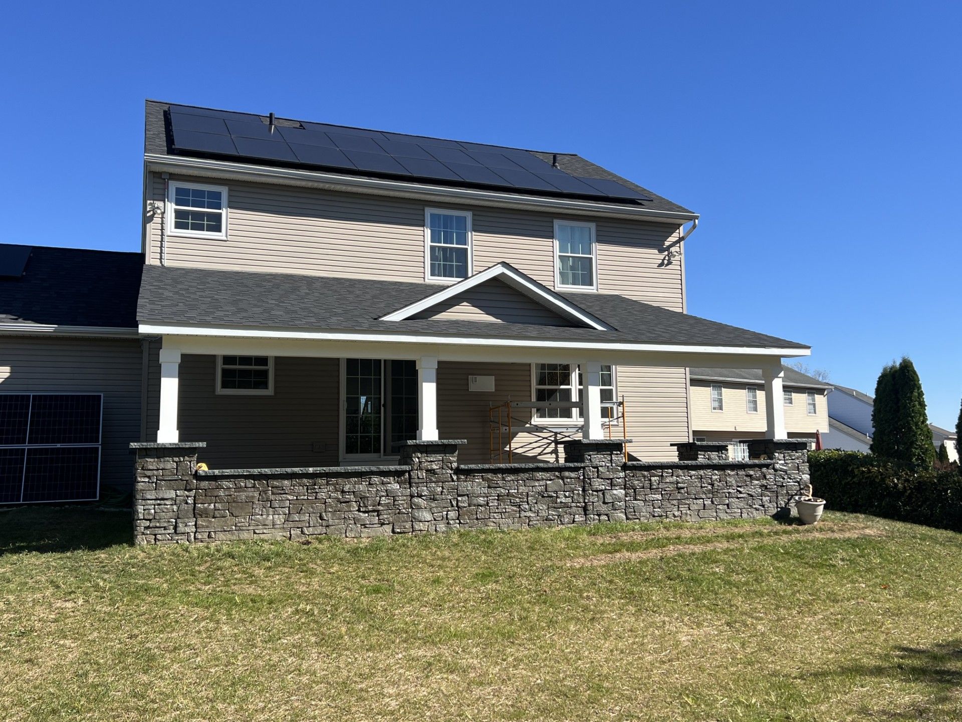 Two-story house with solar panels on the roof and a stone-covered front porch. Sunny day, clear sky.