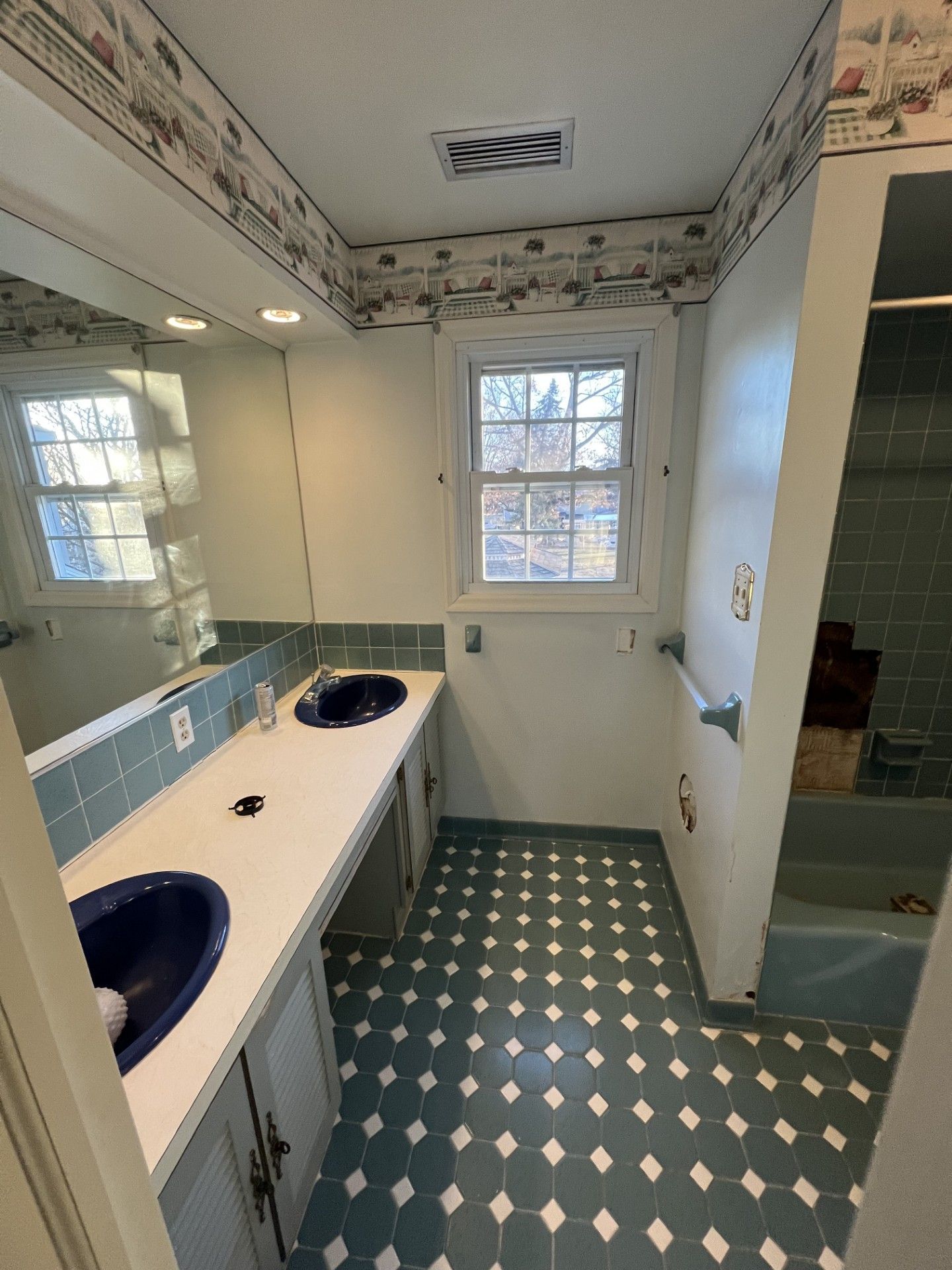 Bathroom with blue tile floor, blue double sinks, and a window.