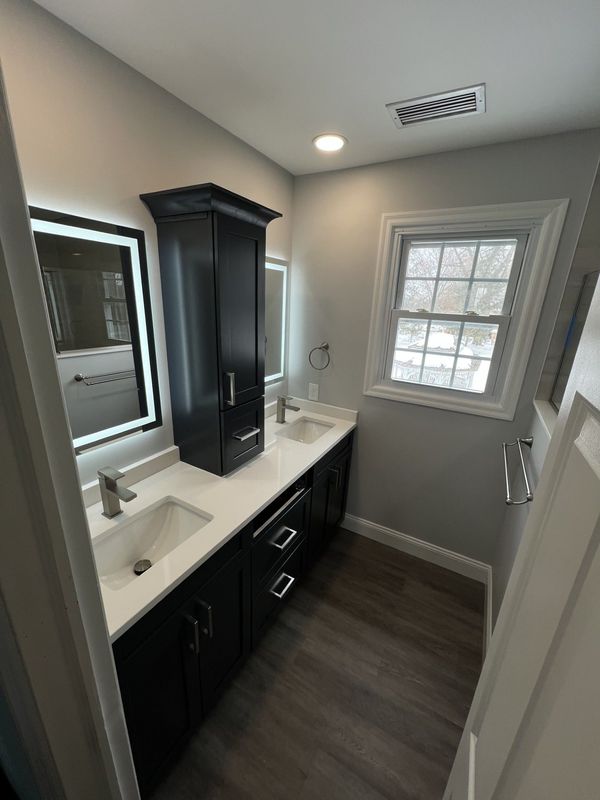 Bathroom with black cabinets, white countertops, and gray walls. Includes a window and a tall storage cabinet.