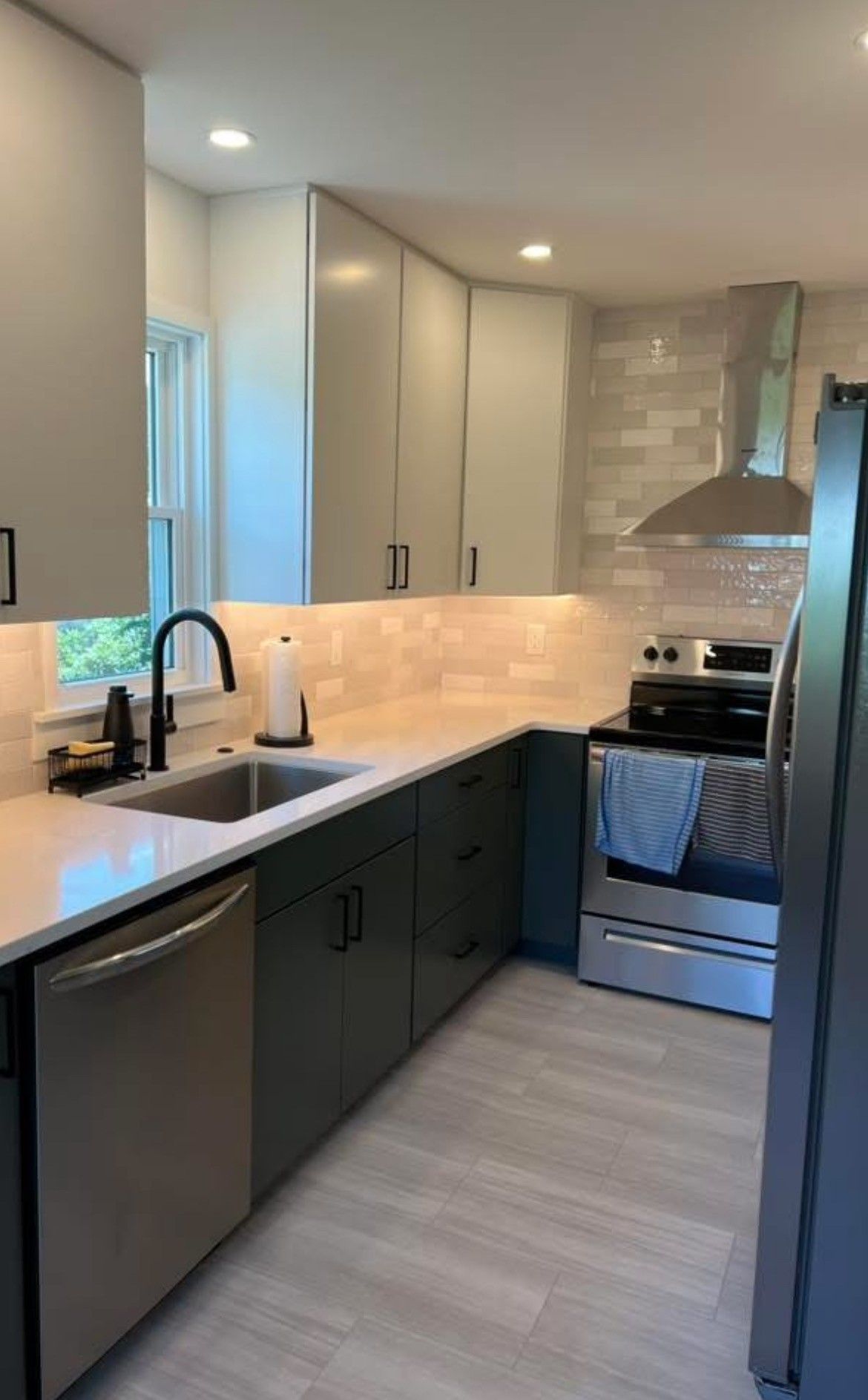 Modern kitchen with gray and white cabinets, stainless steel appliances, and a light-colored tile backsplash.
