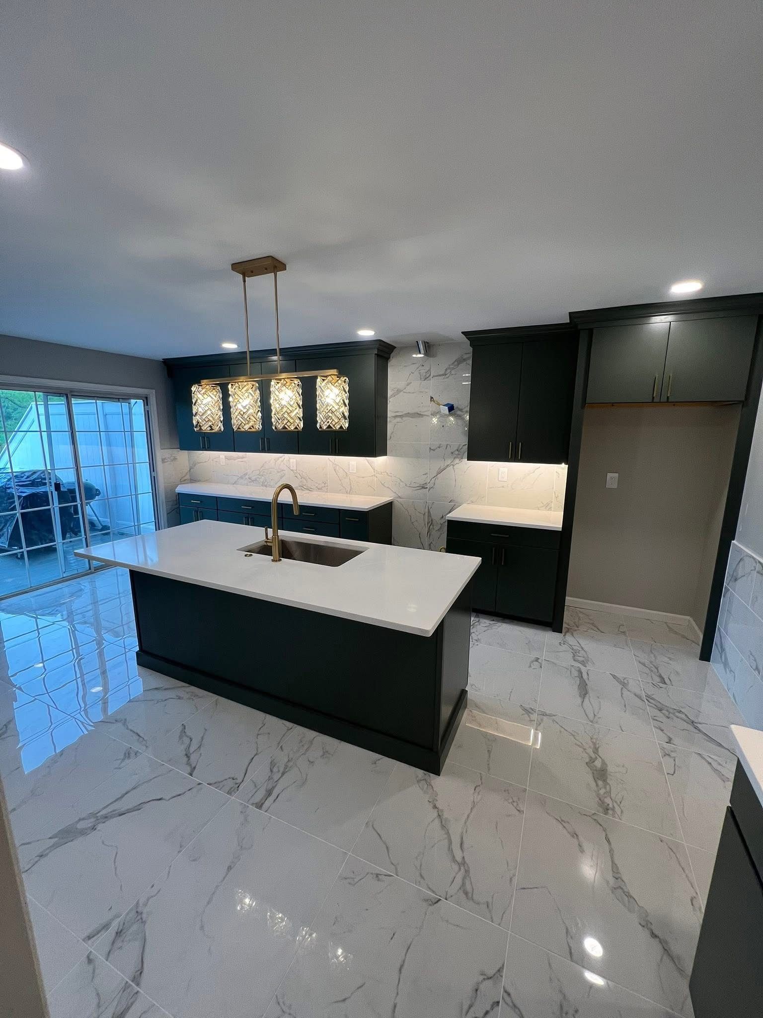 Dark teal and white kitchen with large island, gold accents, and marble-look floors.